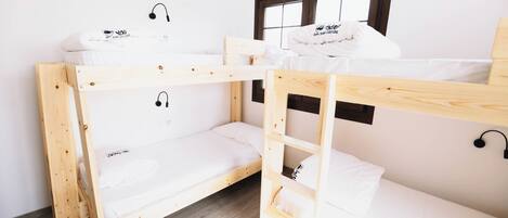 Habitación con literas, ventana, suelo de madera y pared blanca.