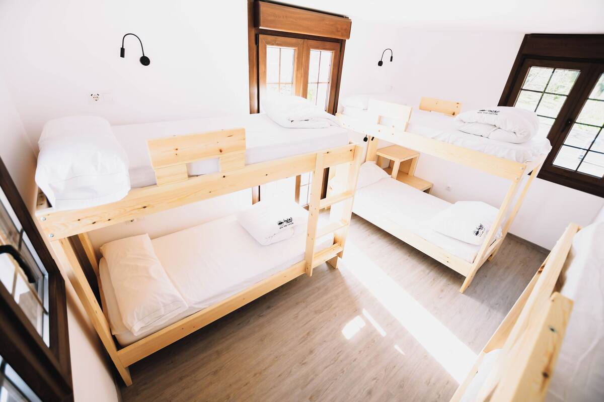 Un dormitorio con literas, un cabecero de madera, una mesita pequeña y una ventana con vistas.