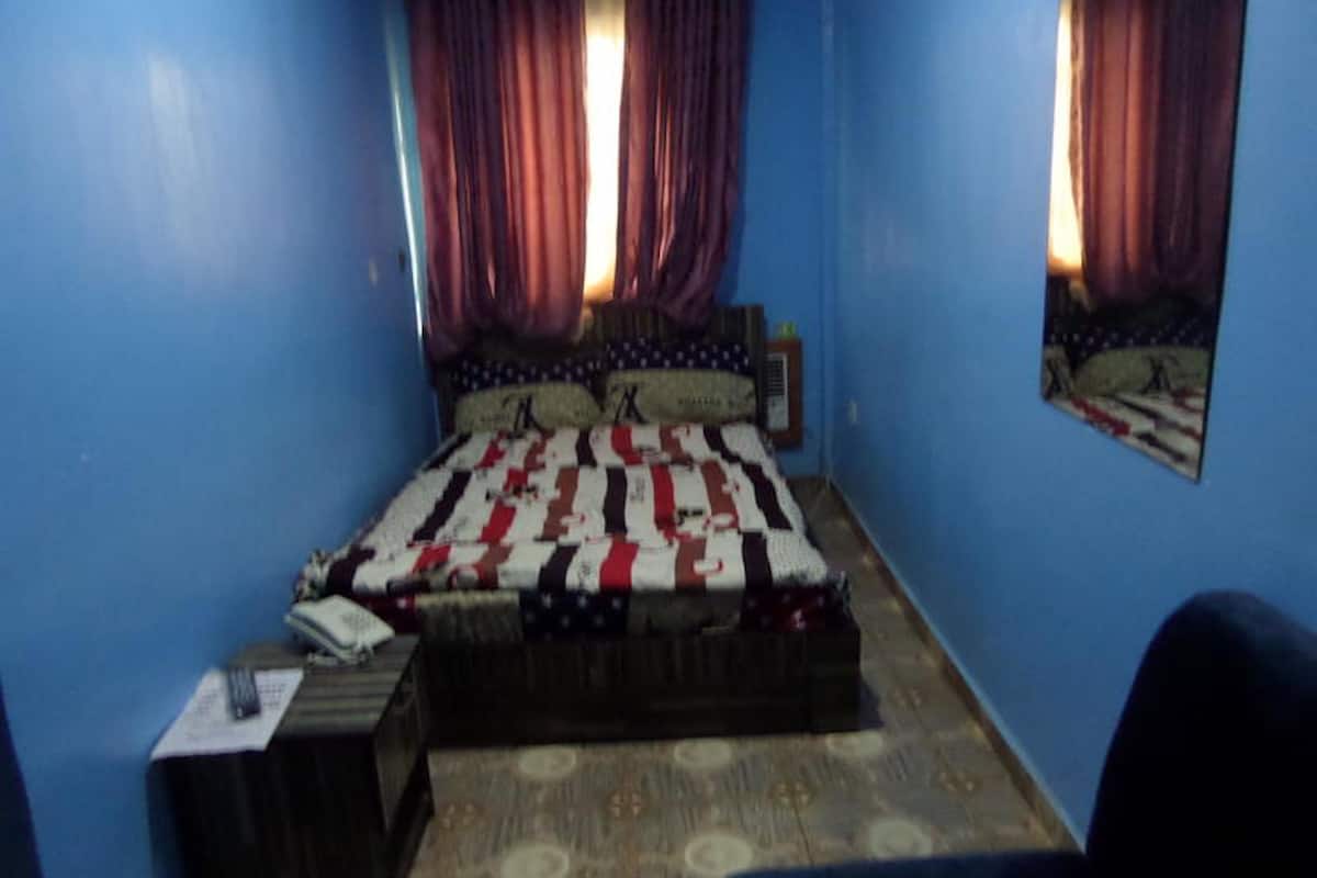 A bedroom with a bed, a nightstand, a chair, and a wall-mounted mirror.