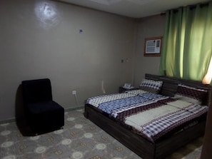A bedroom with a bed, a chair, a nightstand, and a green curtain.