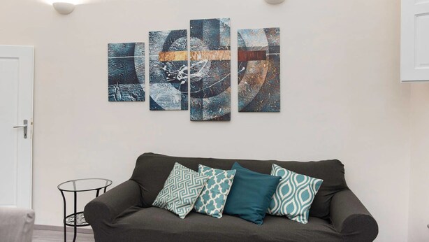 A living room with a dark grey sofa, four patterned cushions, and a wall-mounted abstract art piece. - Porta Rossa (Florence)