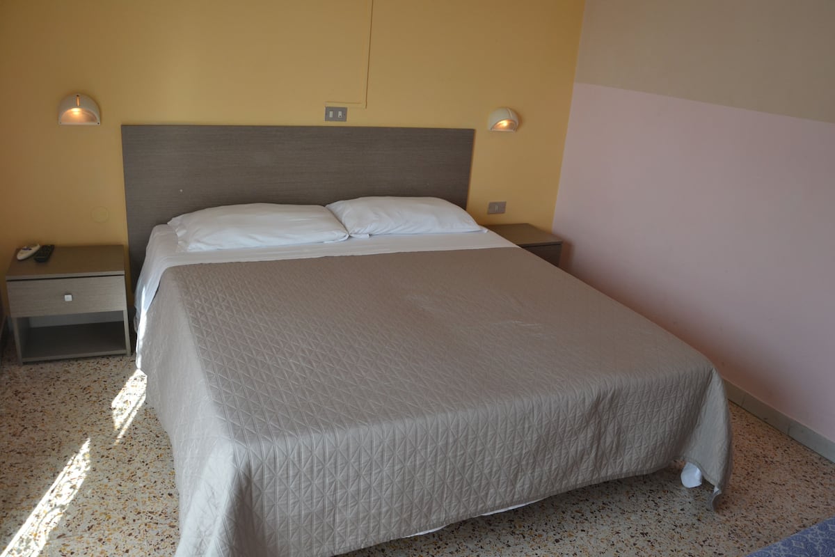 A neatly made bed in a hotel room with a headboard, two bedside tables, and wall-mounted lights.