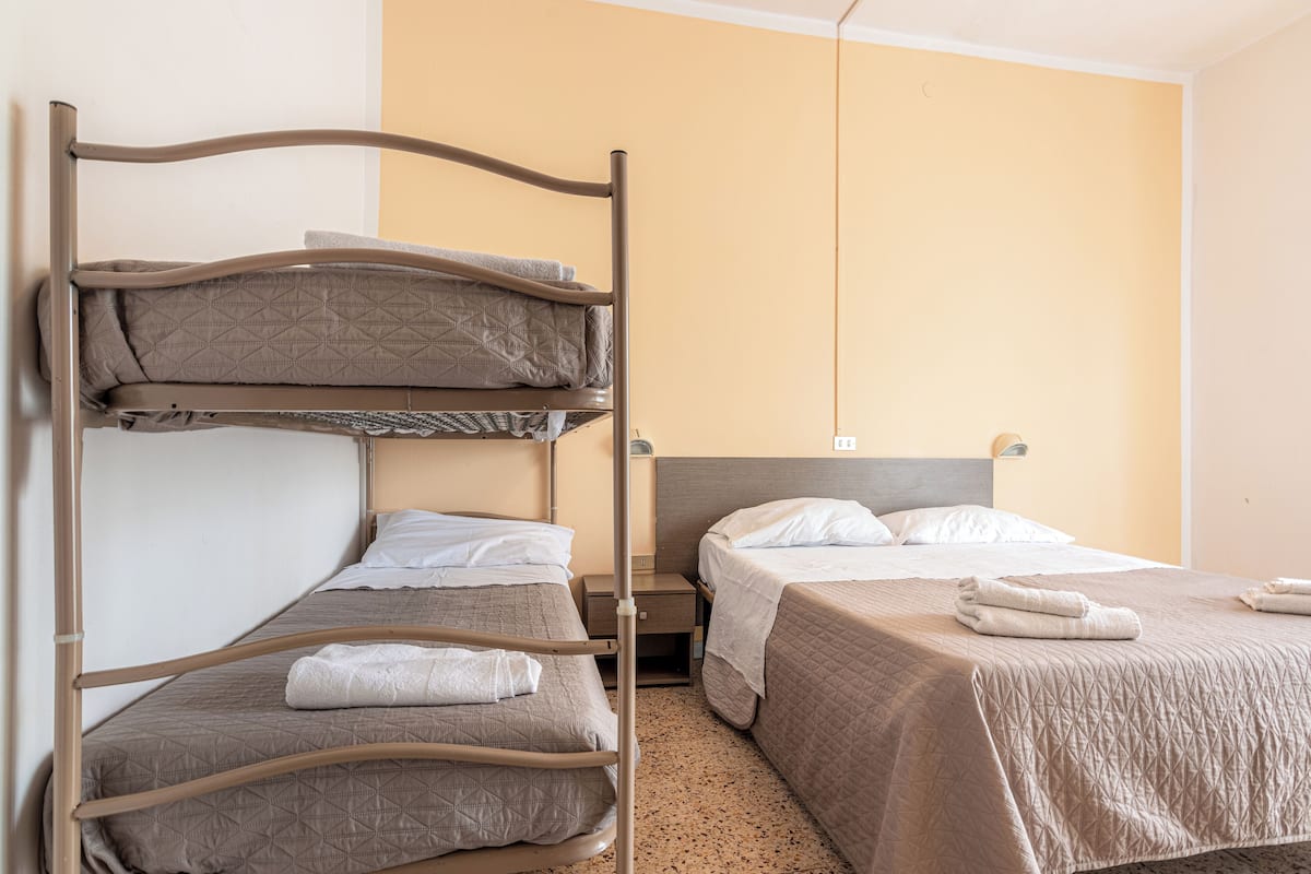 A hotel room with a bunk bed, a single bed, and a nightstand with a lamp.
