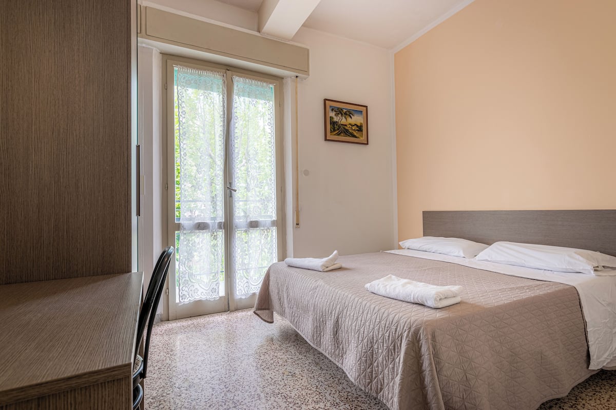 A bedroom with a bed, a chair, a door, and a painting on the wall.