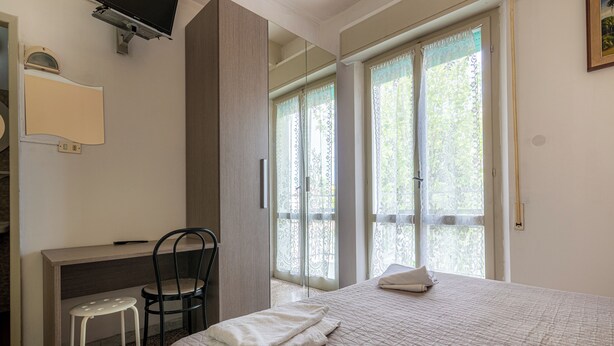 A bedroom with a bed, a desk, a chair, and large windows. - Hotel Britta (Rimini)