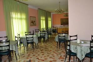 A dining area with multiple tables and chairs, green curtains, and a patterned floor. - Hotel Britta (Rimini)