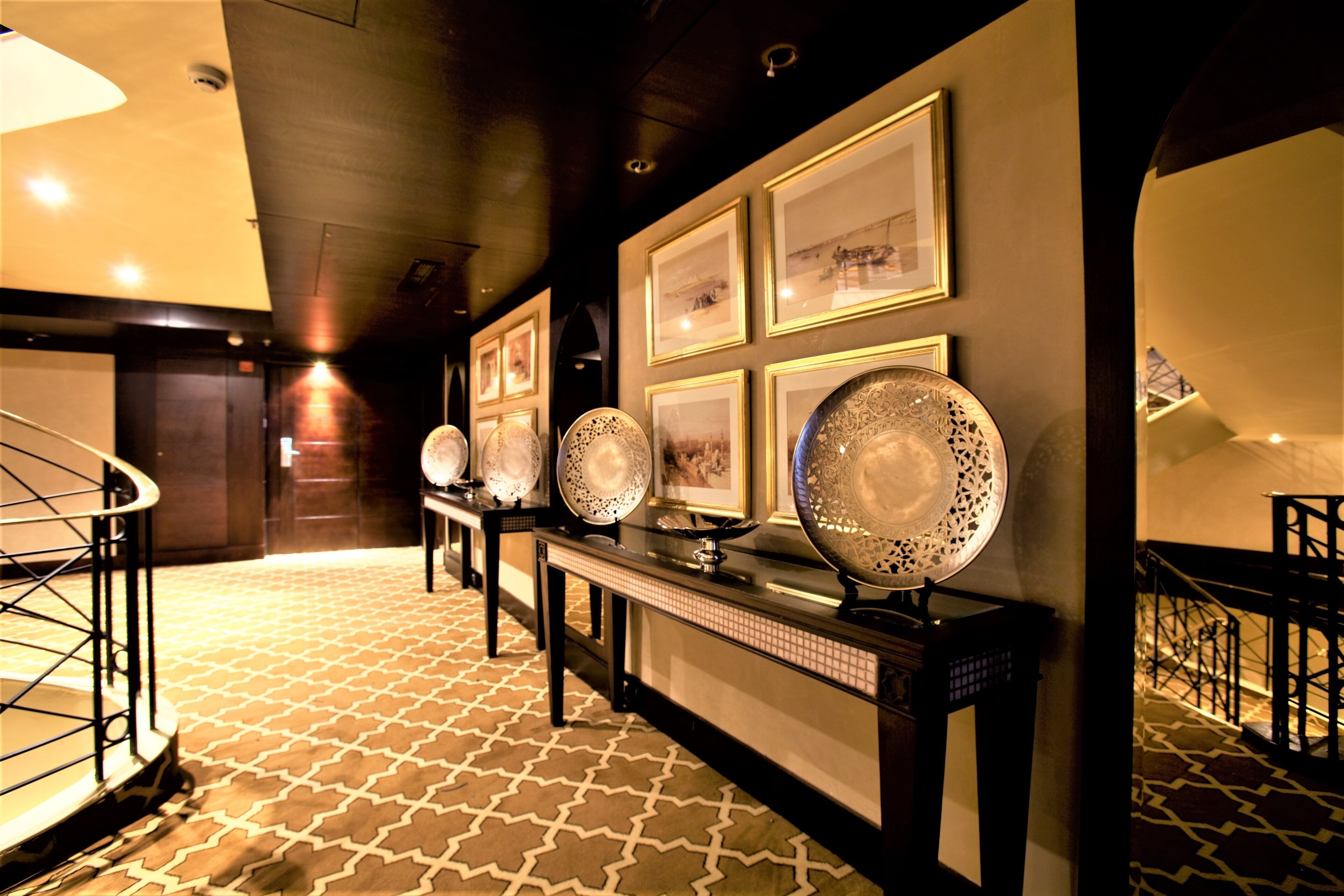A hallway with patterned carpet, a staircase, and a wall adorned with framed pictures and decorative plates.