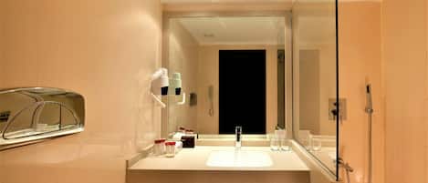 A modern bathroom with a large mirror, a sink, a shower, and a hairdryer mounted on the wall.