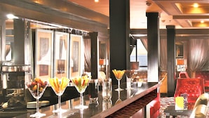A bar area with a long counter, multiple glasses of beverages, and a seating area with red upholstered chairs.