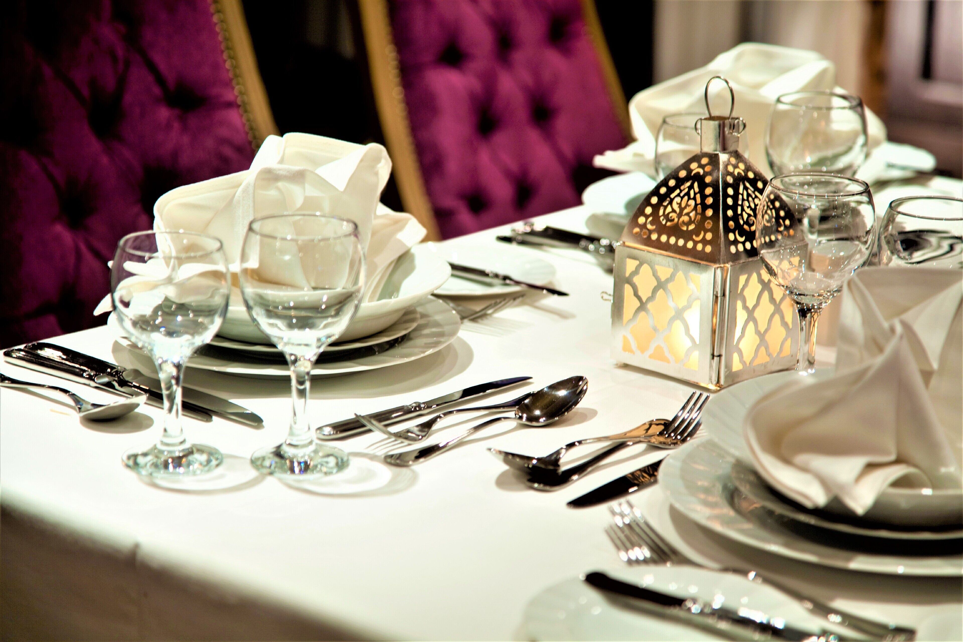 A table set for a formal dining experience with white tablecloths, silverware, and clear glassware.