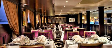 A restaurant with multiple tables set for dining, featuring plush seating and a patterned floor.