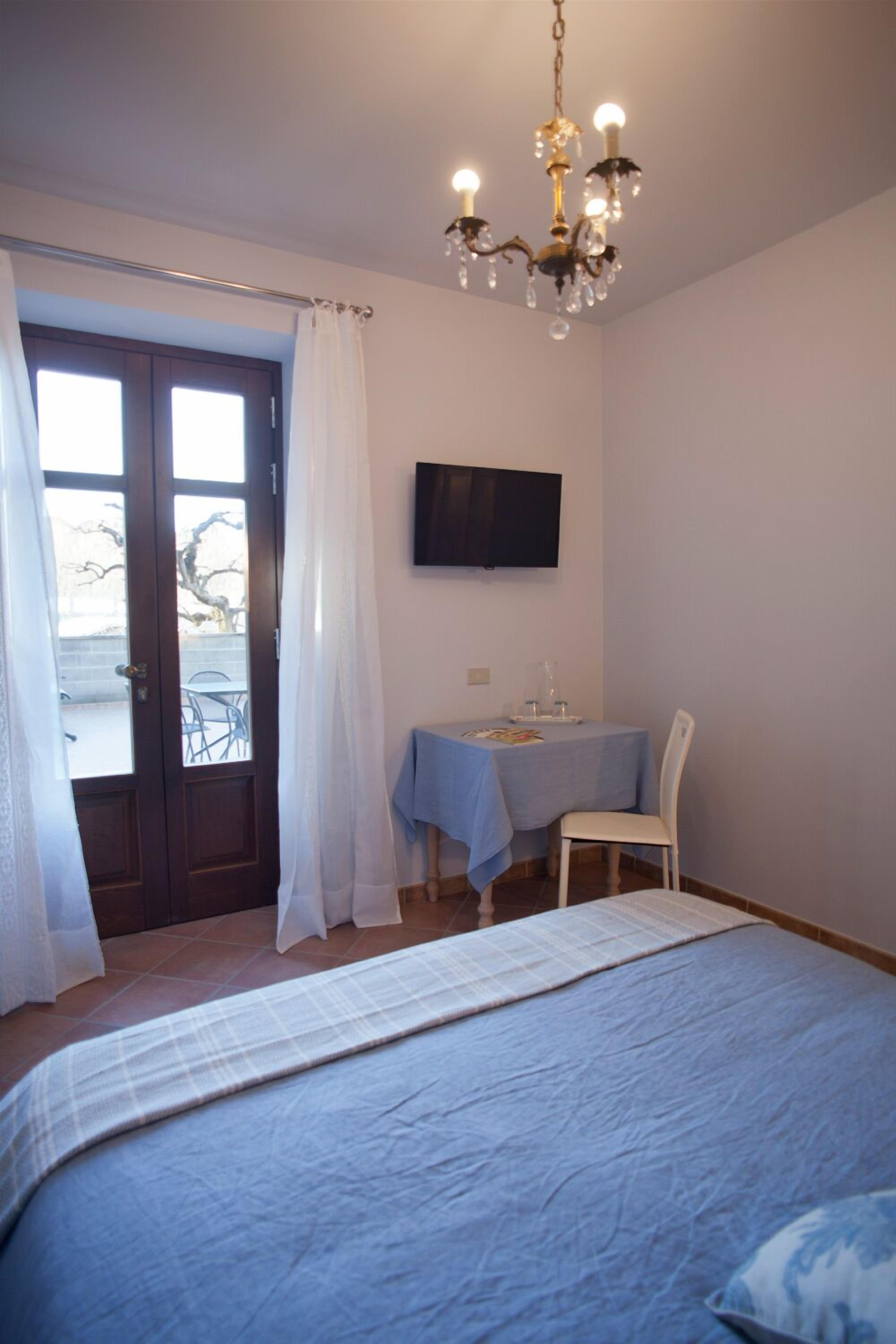 Una camera da letto con un letto, una scrivania con una sedia, una TV appesa al muro e una finestra con tende.