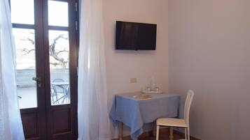 Una camera da letto con un letto, una scrivania con una sedia, una TV appesa al muro e una finestra con tende.