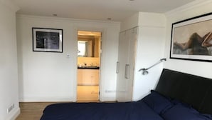 Une chambre à coucher avec un grand lit, une armoire, une porte donnant sur une salle de bain et un tableau encadré au mur.