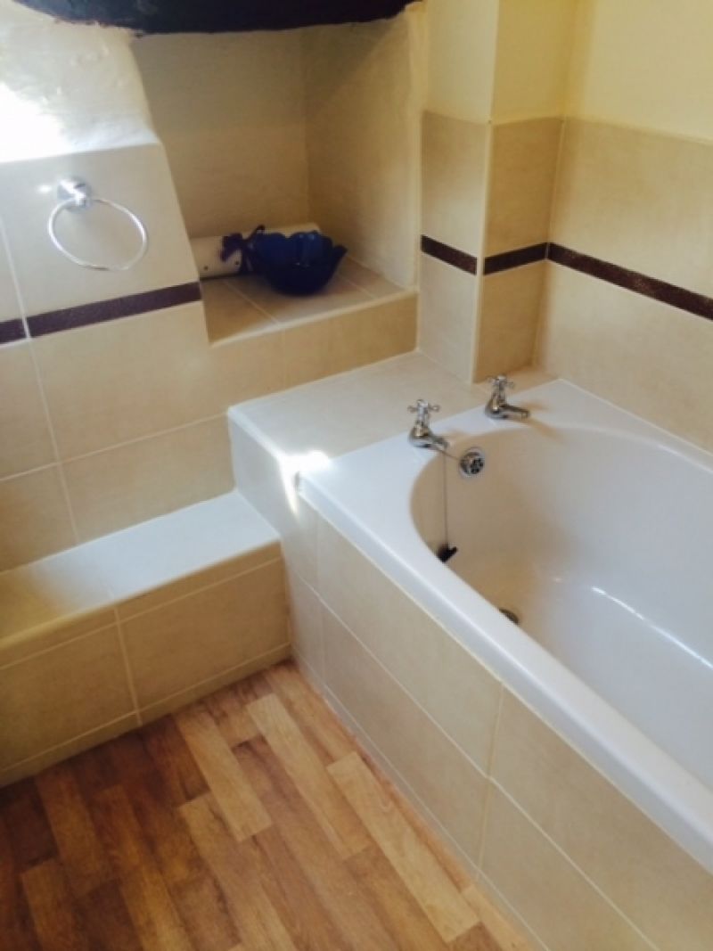 A bathroom with a bathtub, a towel ring, and a shelf with a blue bag.