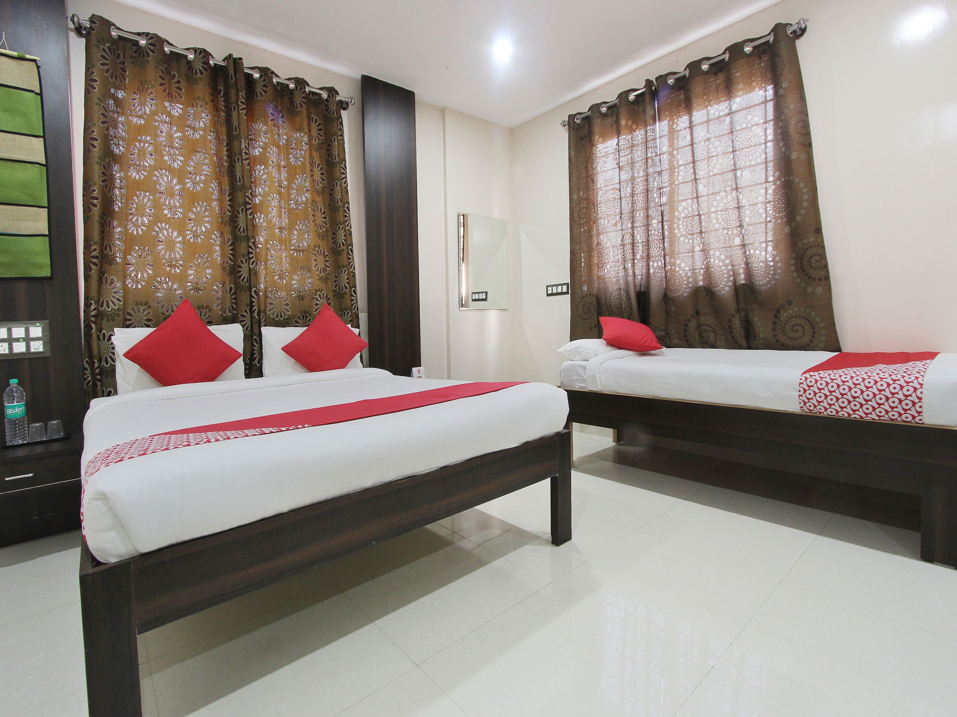 A hotel room with two beds, each with a red pillow and a patterned bedspread.