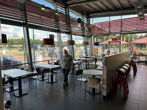 Un comedor interior con mesas y sillas, ventanas grandes y vistas al estacionamiento exterior.