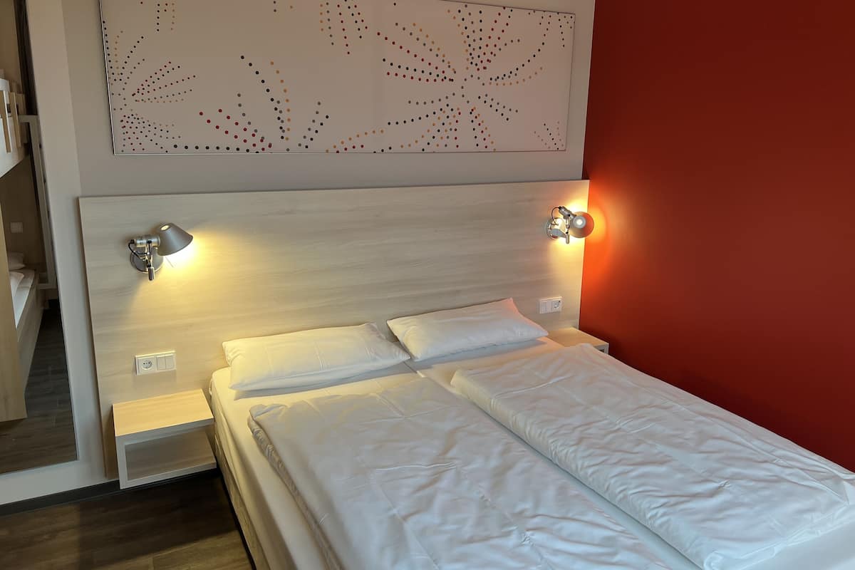 A neatly made bed with two pillows, a wooden headboard, and two wall-mounted reading lamps.
