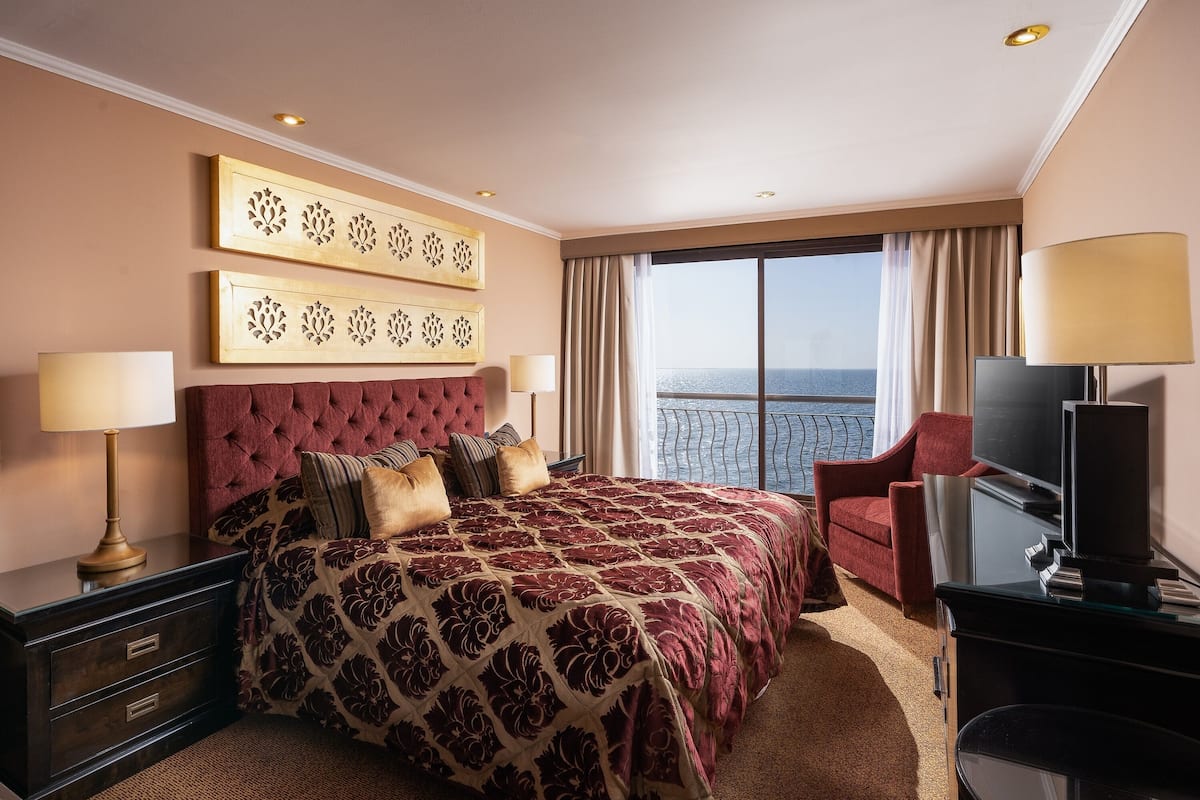Ett hotellrum med en stor säng, en TV, ett skrivbord och utsikt över havet.