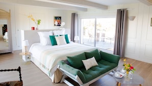 A modern bedroom with a bed, a green sofa, a small table with cups and a vase of flowers, and a sliding glass door to a balcony. - Les Hauts d'Etretat (Bordeaux-Saint-Clair)