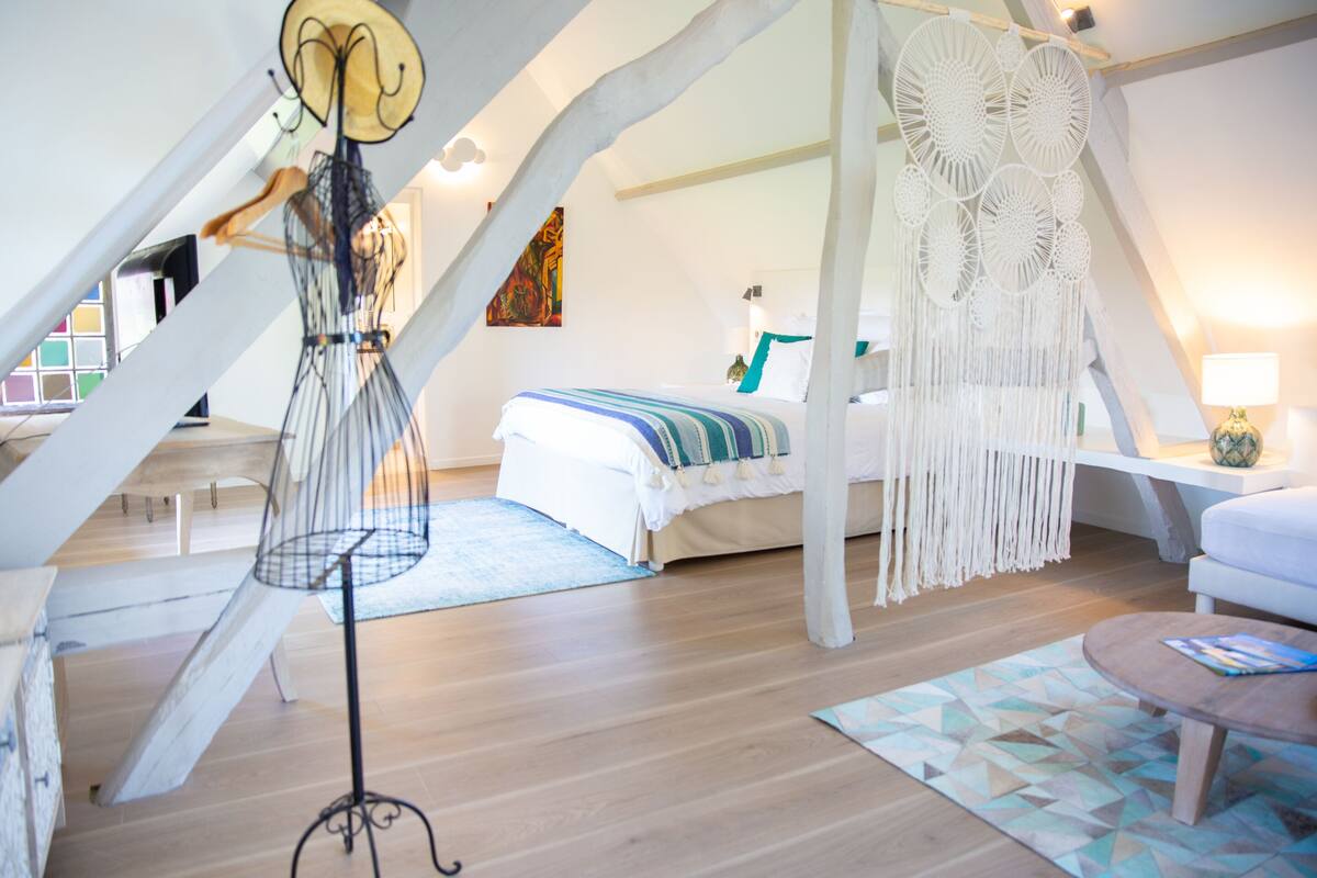 A bedroom with a bed, a hanging chair, a macrame wall hanging, and a wooden floor.