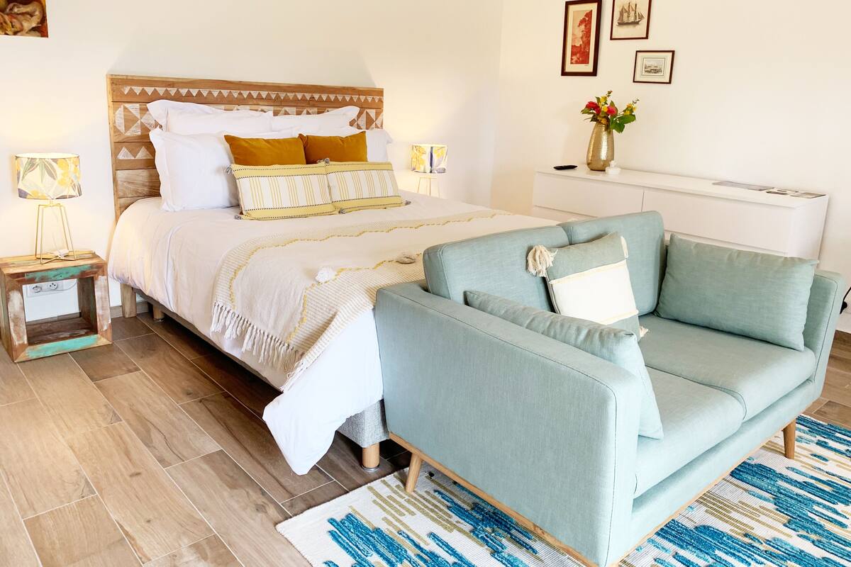 A bedroom with a bed, a sofa, a nightstand, a lamp, and a vase with flowers.