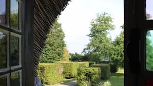A view from a window with a thatched roof, overlooking a well-maintained garden with hedges and trees. - Les Hauts d'Etretat (Bordeaux-Saint-Clair)