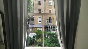 A view through a window with curtains, revealing a multi-story building with balconies and greenery outside. - Eson2 - The Kensington Gwendwr Road Lodge (London)