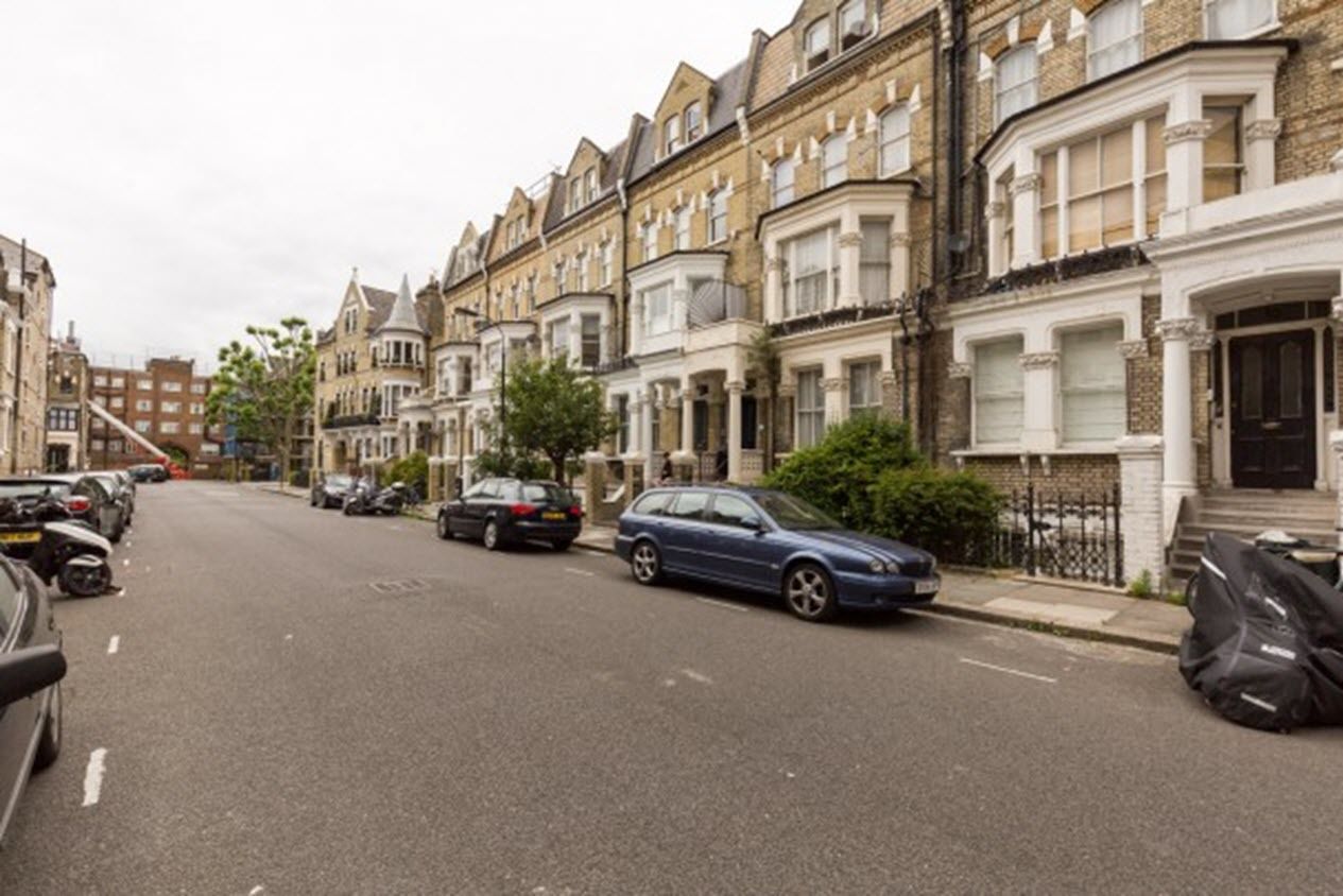 A street lined with terraced houses, parked cars, and a clear road.
