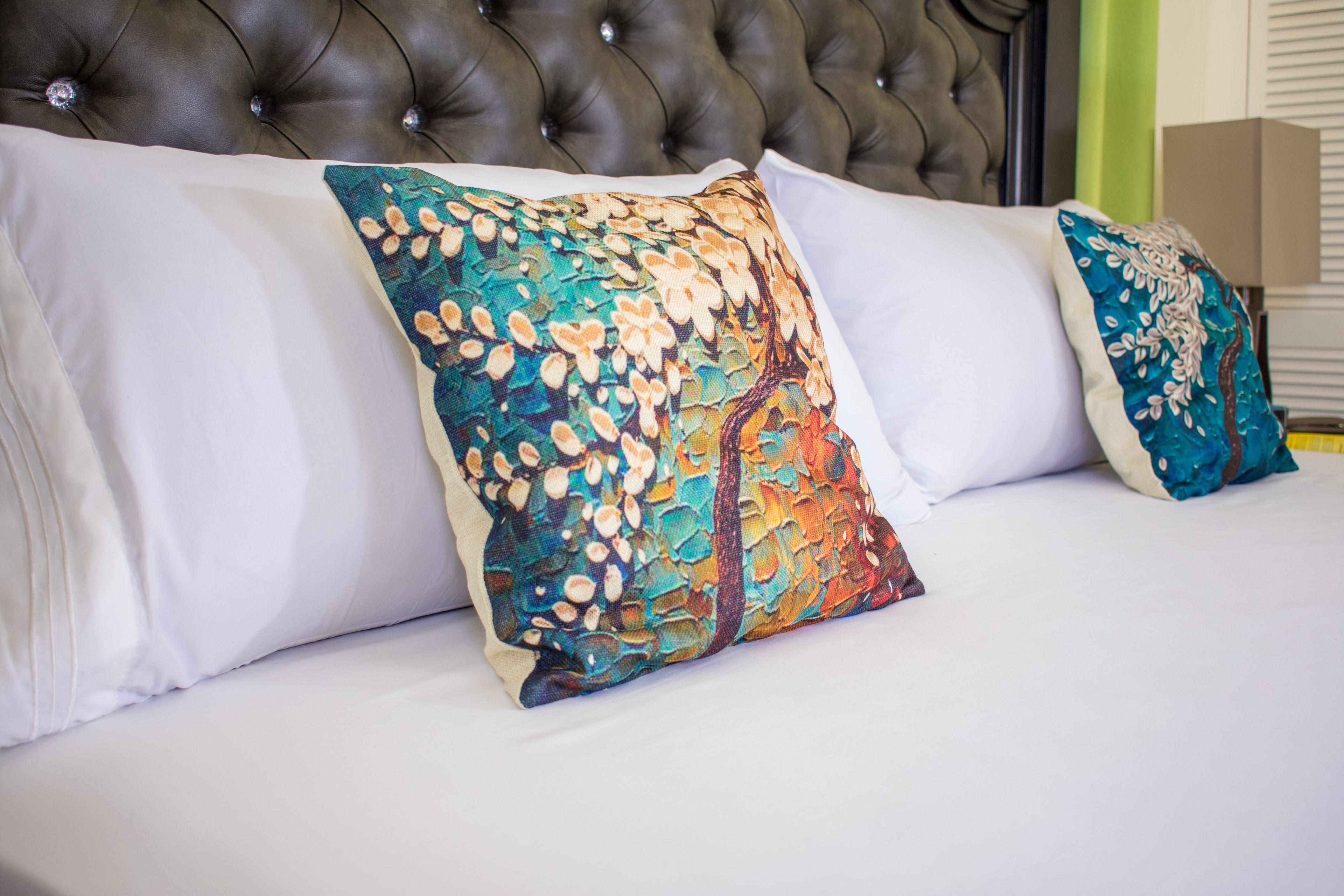 A bed with white and colorful pillows, a tufted headboard, and a plain wall.