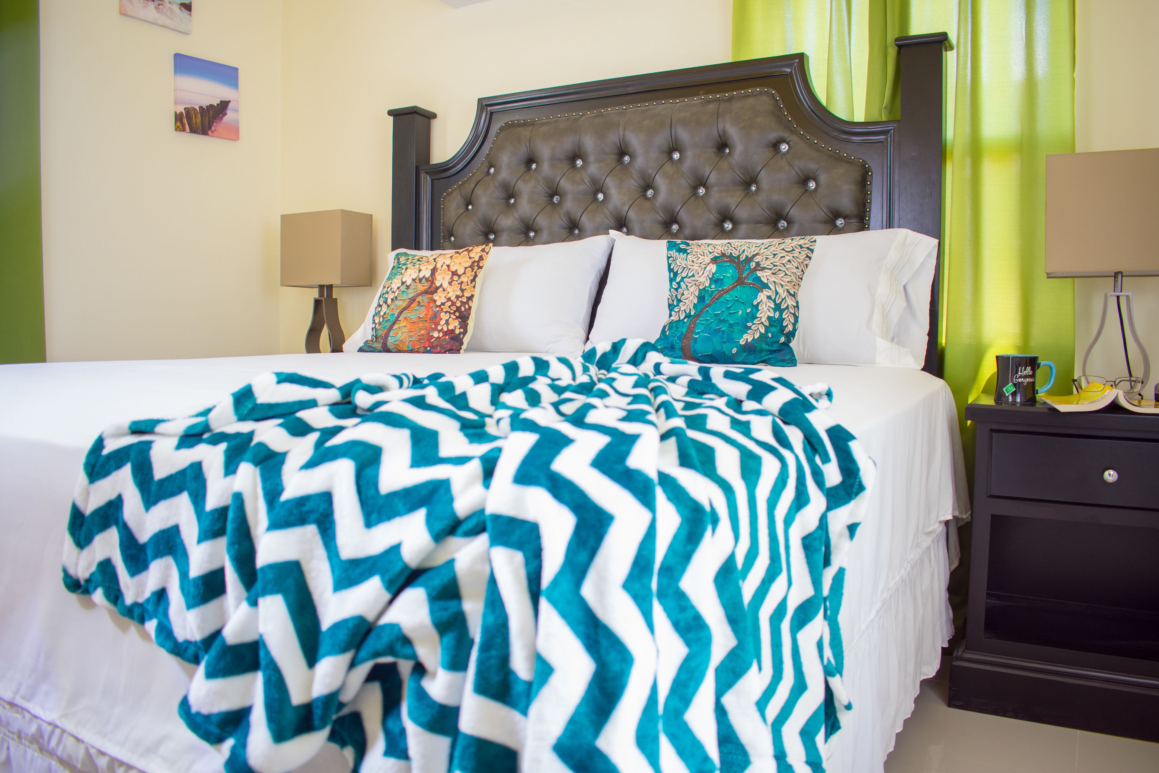Un lit bien fait, avec une couverture à motifs, une tête de lit sombre et des coussins décoratifs.