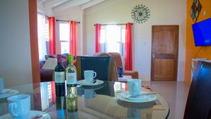 A dining area with a glass table, chairs, and a television on a stand. - Drax Hall Manor Country Club Villa (Ocho Rios)
