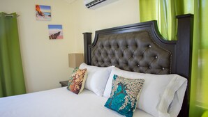 A neatly made bed with a tufted headboard, two decorative pillows, and a green curtain. - Drax Hall Manor Country Club Villa (Ocho Rios)