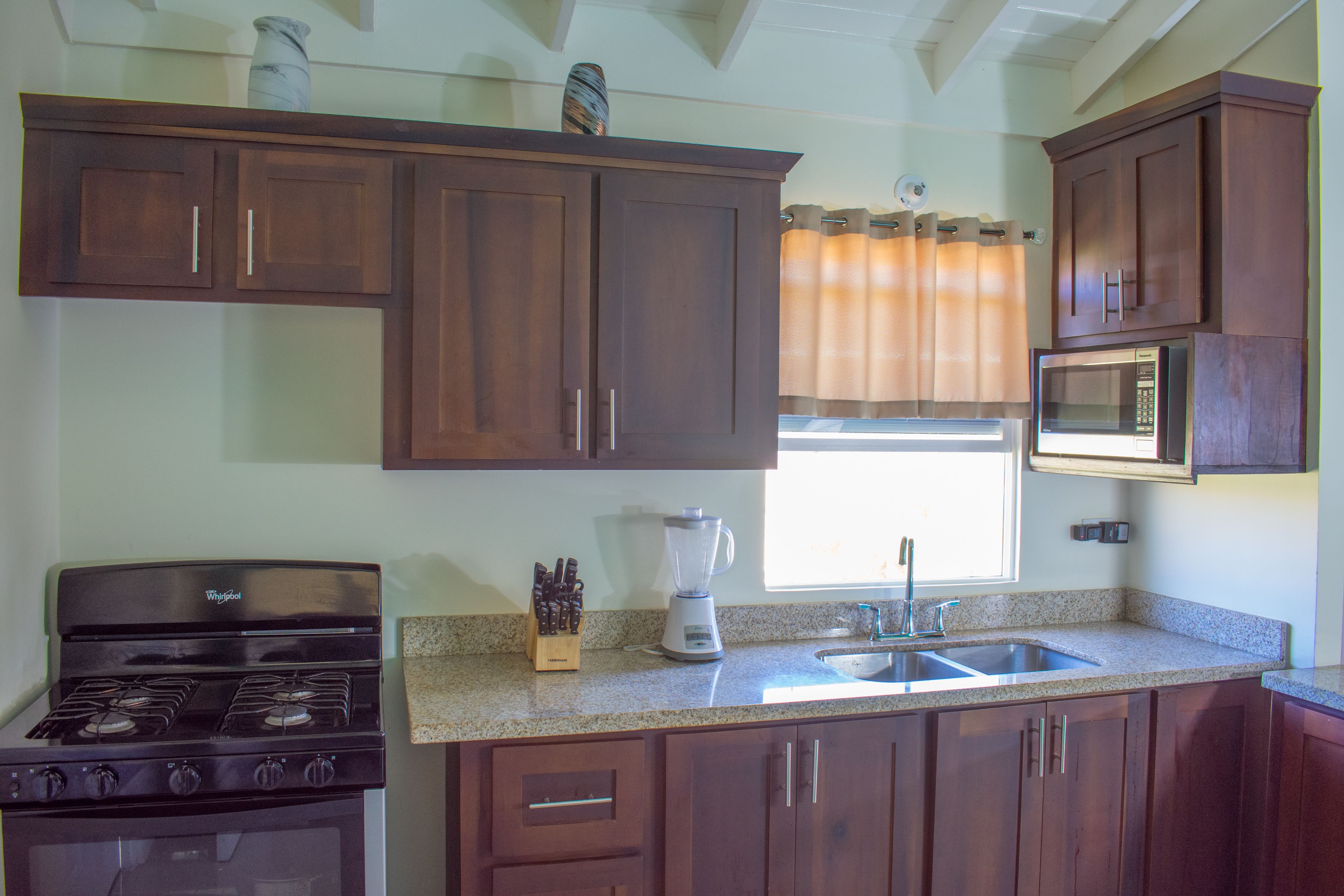 A kitchen with wooden cabinets, a stove, a sink, and a microwave.
