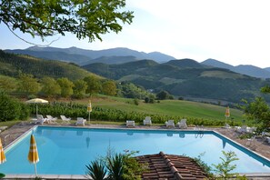 A swimming pool with lounge chairs and umbrellas, surrounded by a landscaped garden and a view of rolling hills and mountains.