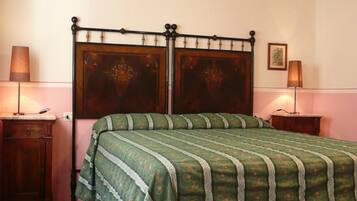 A bedroom with a wooden ceiling, a bed with a green patterned bedspread, two bedside tables with lamps, and a framed picture on the wall.