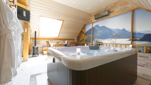 A spa room with a hot tub, wooden walls, a large window, and a mountain view painting. - La Ferme Briarde (Augers-en-Brie)