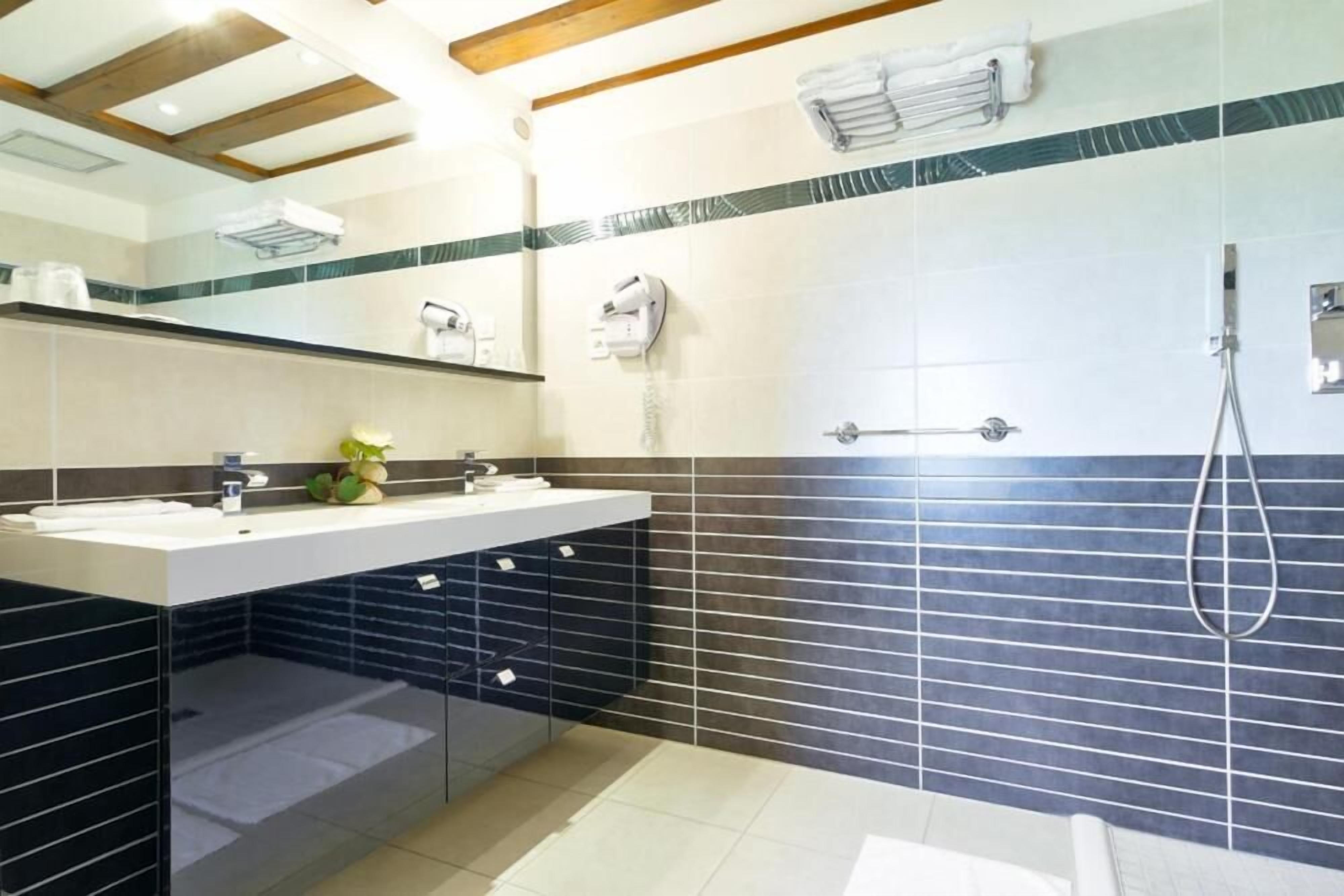 Ein modernes Badezimmer mit großem Spiegel, Waschbecken, Dusche und Handtuchhalter.