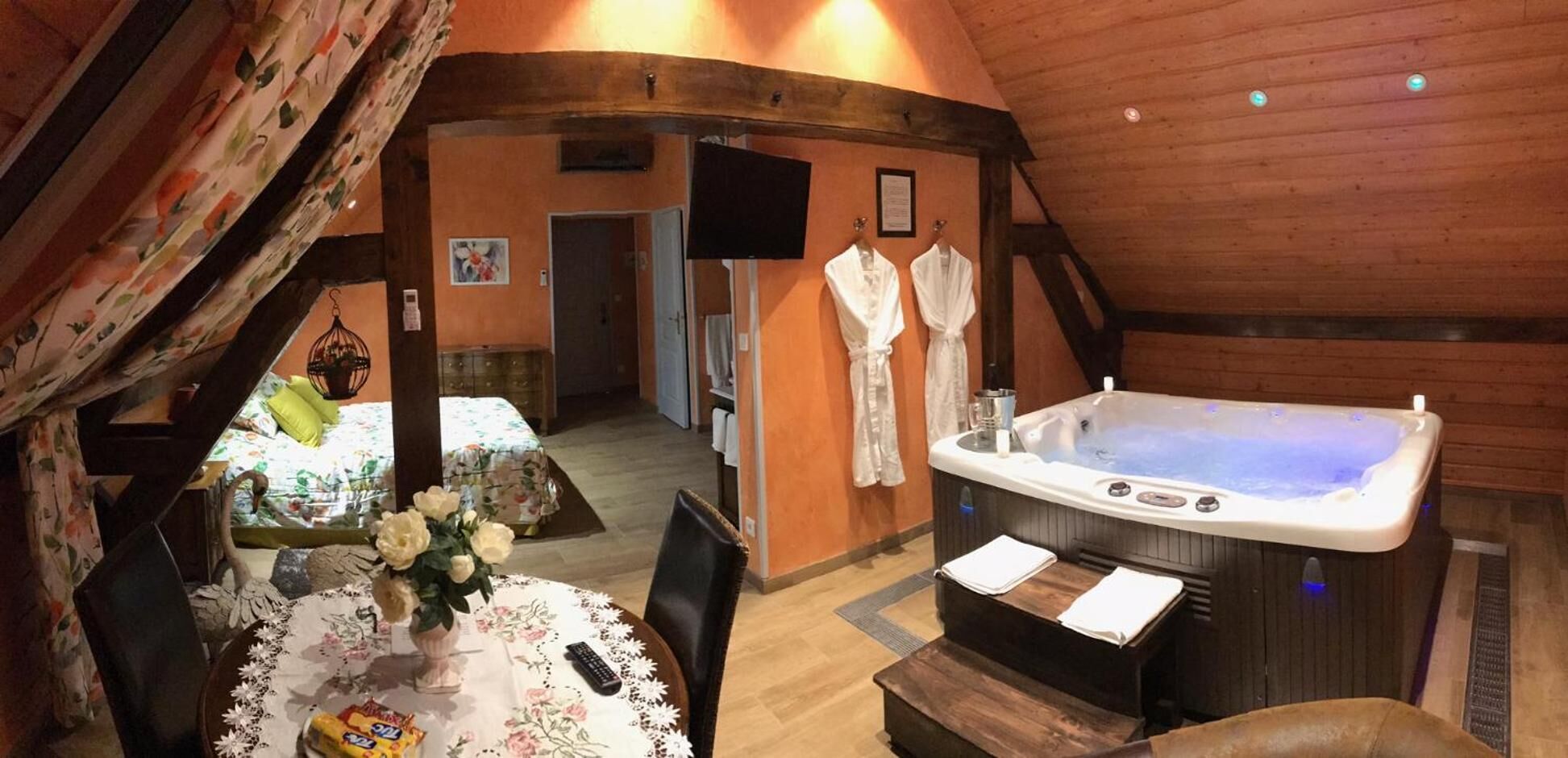 A cozy room with a wooden ceiling, a hot tub, a dining table with chairs, and a bed with floral bedding.