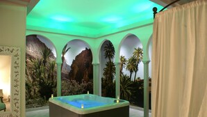 A spa room with a hot tub, arched columns, and tropical wall murals. - La Ferme Briarde (Augers-en-Brie)