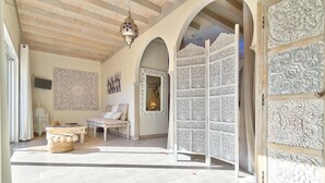 A room with a high ceiling, a hanging light fixture, a sofa, a decorative screen, and a patterned wall. - La Ferme Briarde (Augers-en-Brie)