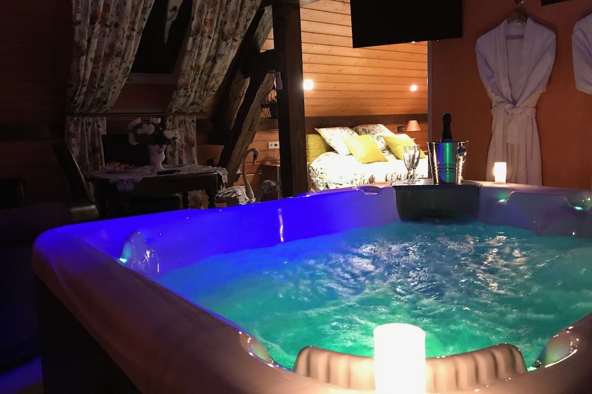 A room with a hot tub, wooden walls, a bed with floral bedding, and a robe hanging on the wall.