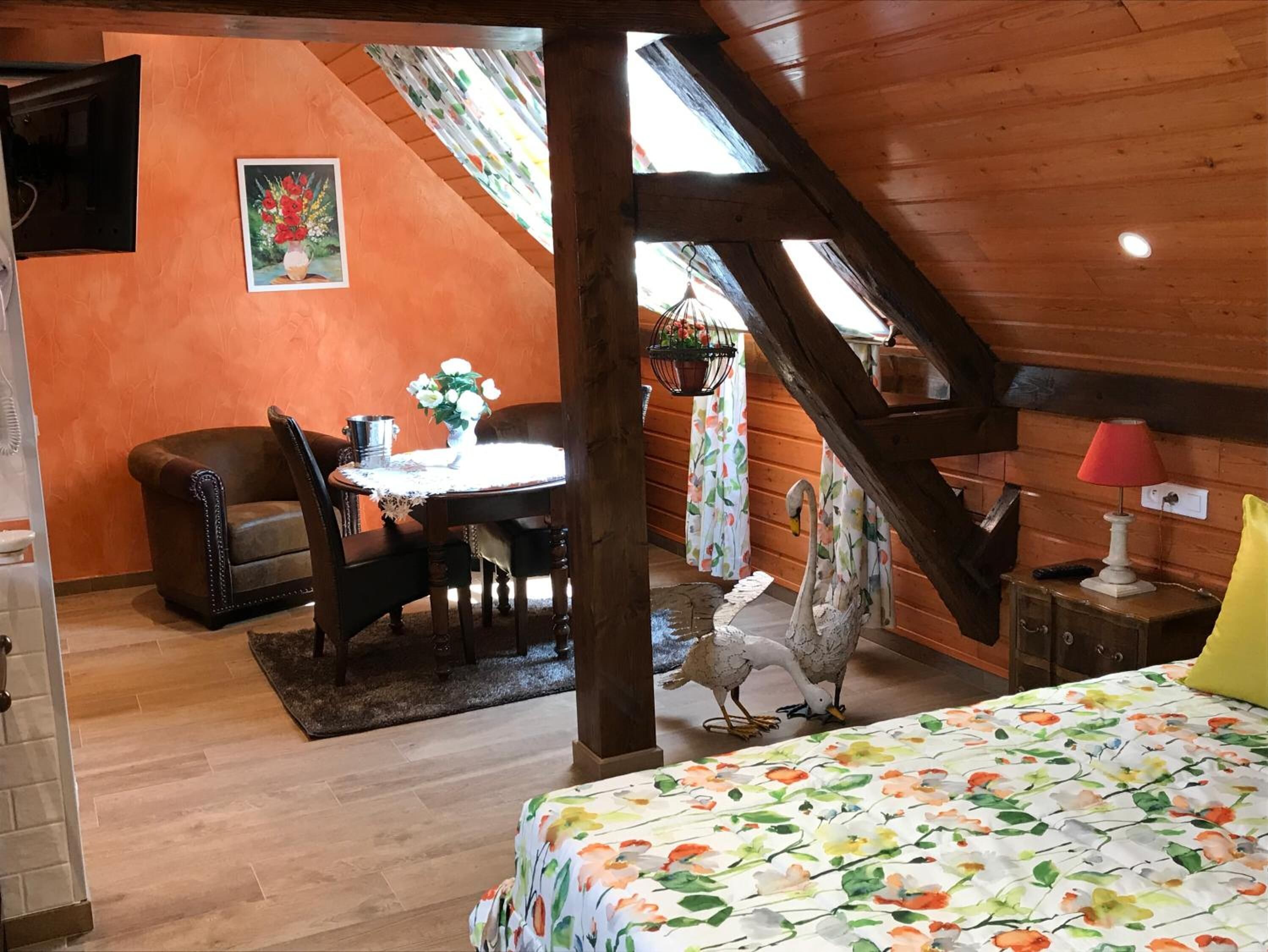 A cozy room with a wooden ceiling, a dining area with a table and chairs, a bed with a floral bedspread, and a swan decoration.
