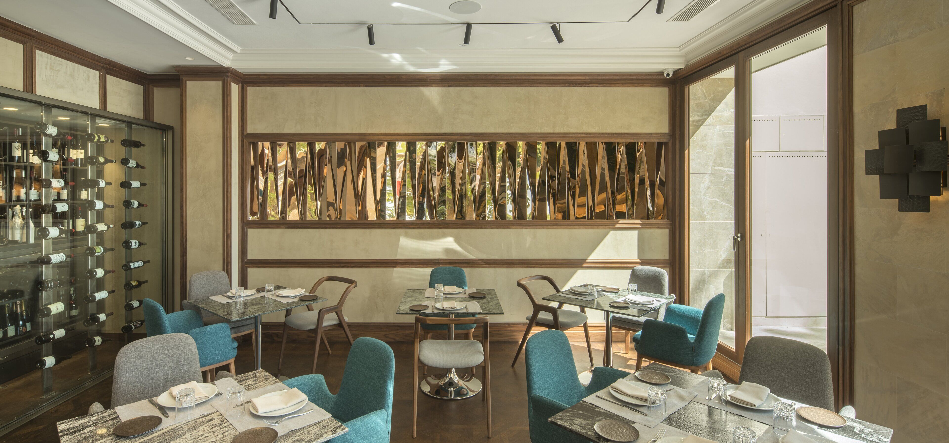 Zona pranzo con diversi tavoli e sedie, una credenza per vini e un pannello decorativo con listelli verticali.