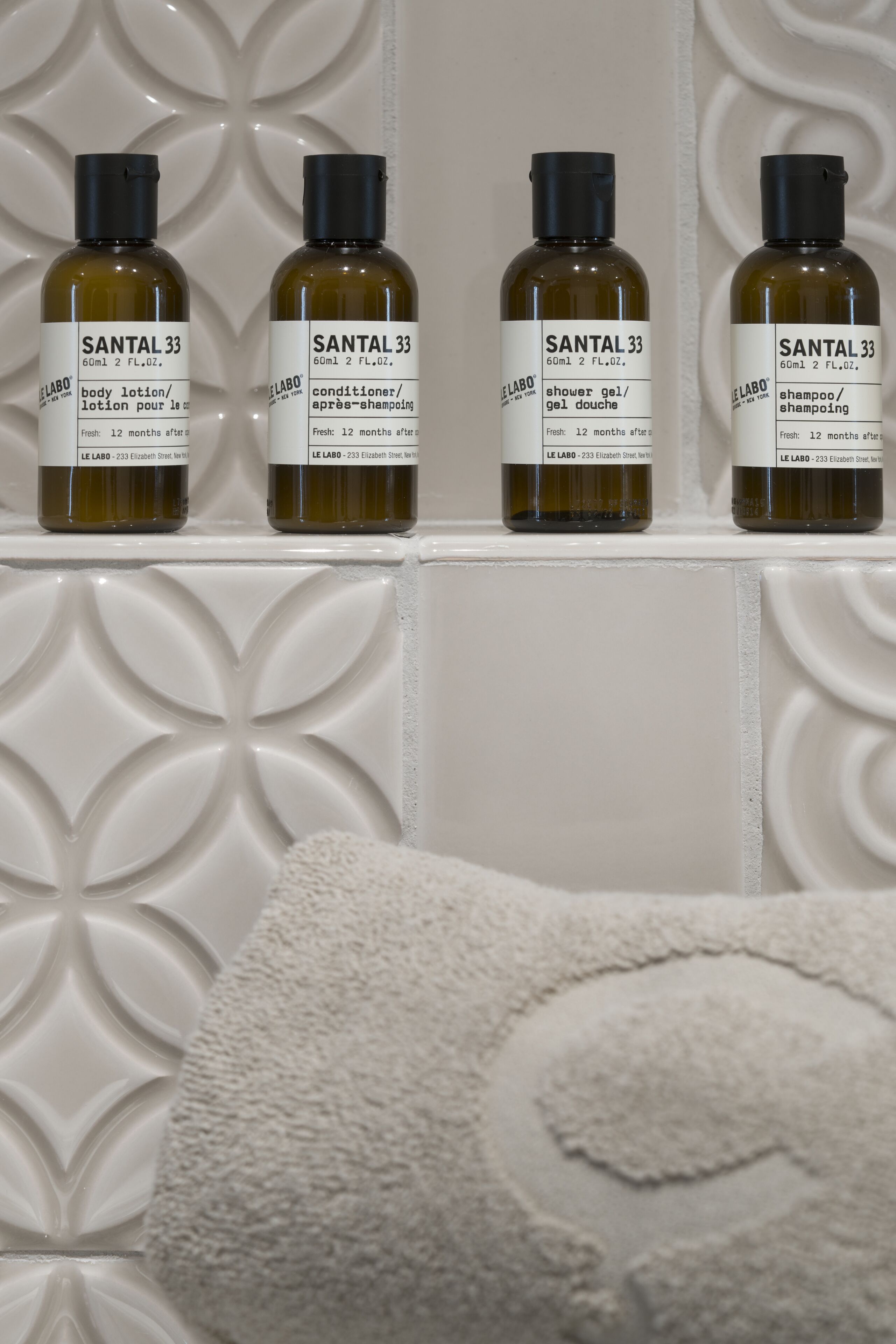 Cuatro botellas de loción corporal Santal 33 sobre una estantería.