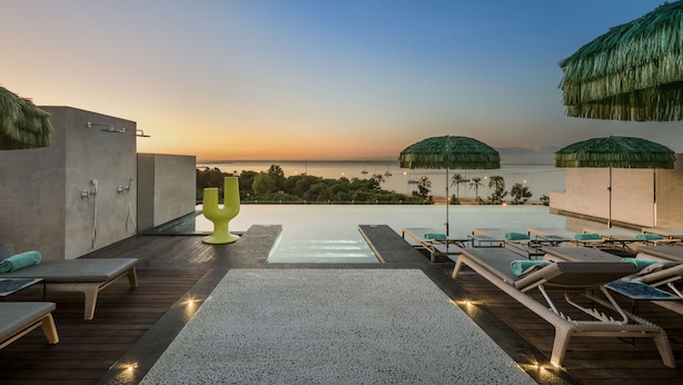 A rooftop infinity pool with lounge chairs and a cactus-shaped sculpture, overlooking a body of water at sunset. - Hotel El Llorenç Parc de la Mar - Adults Only (Palma de Mallorca)
