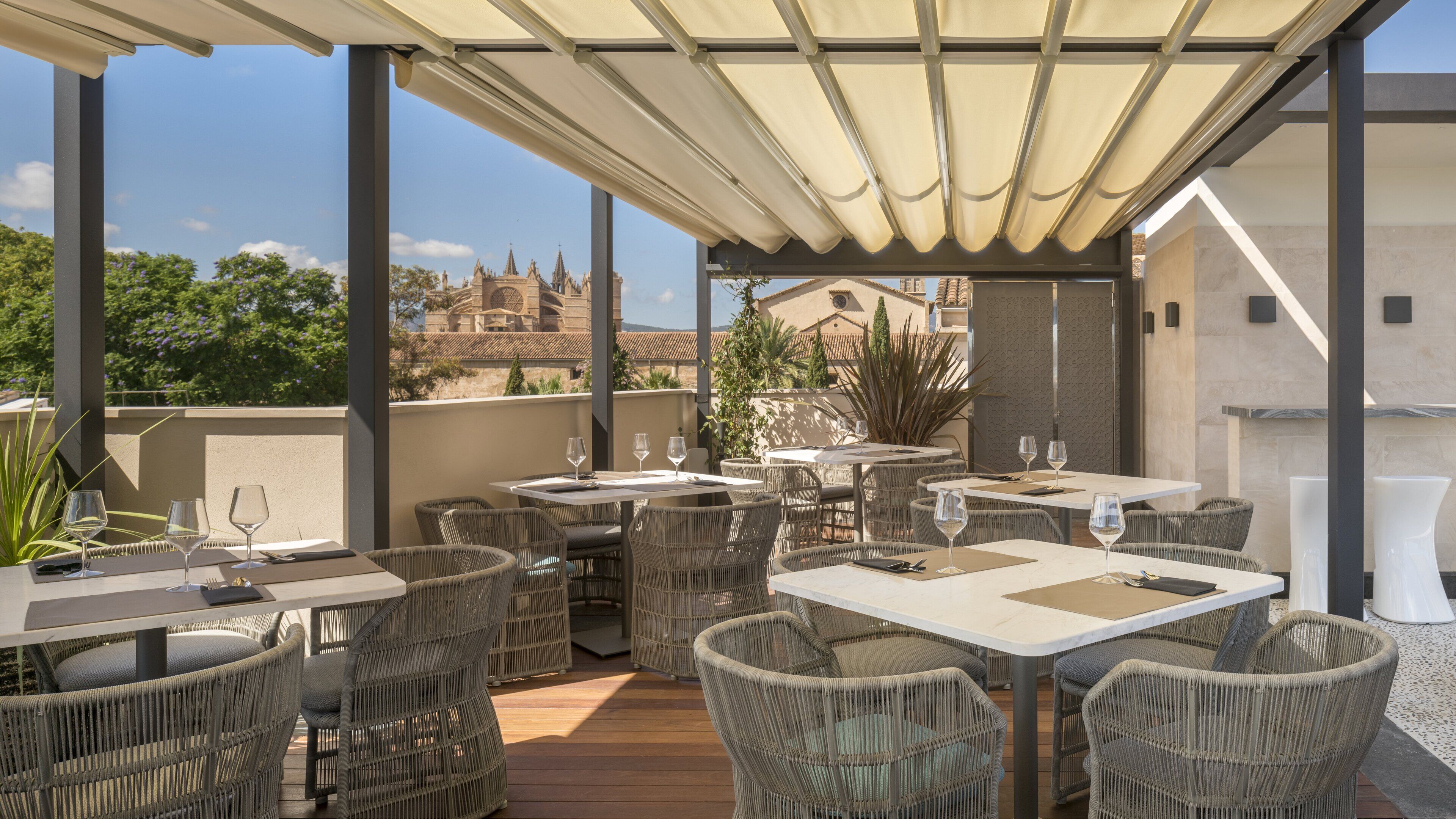 An outdoor patio with wicker furniture and tables, a pergola overhead, and a view of a historic building in the background.