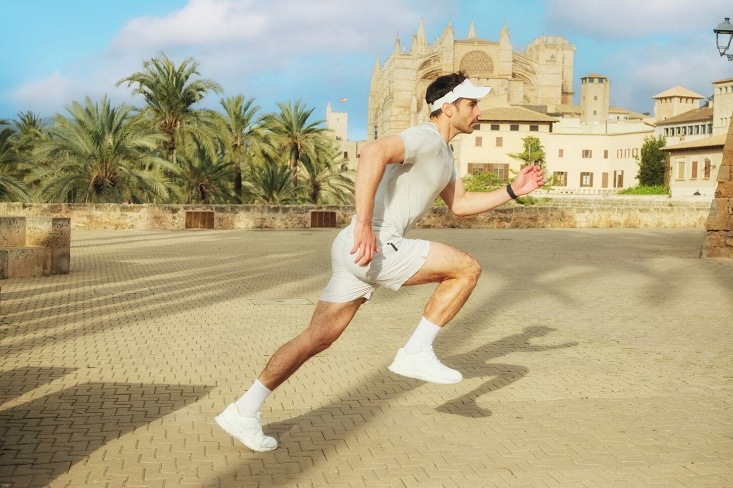 Eine Person joggt auf einer gepflasterten Fläche, im Hintergrund sind Palmen und ein historisches Gebäude zu sehen.