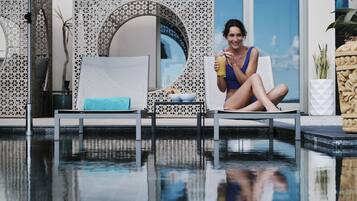 A poolside area with lounge chairs, a person holding a drink, and a decorative wall.