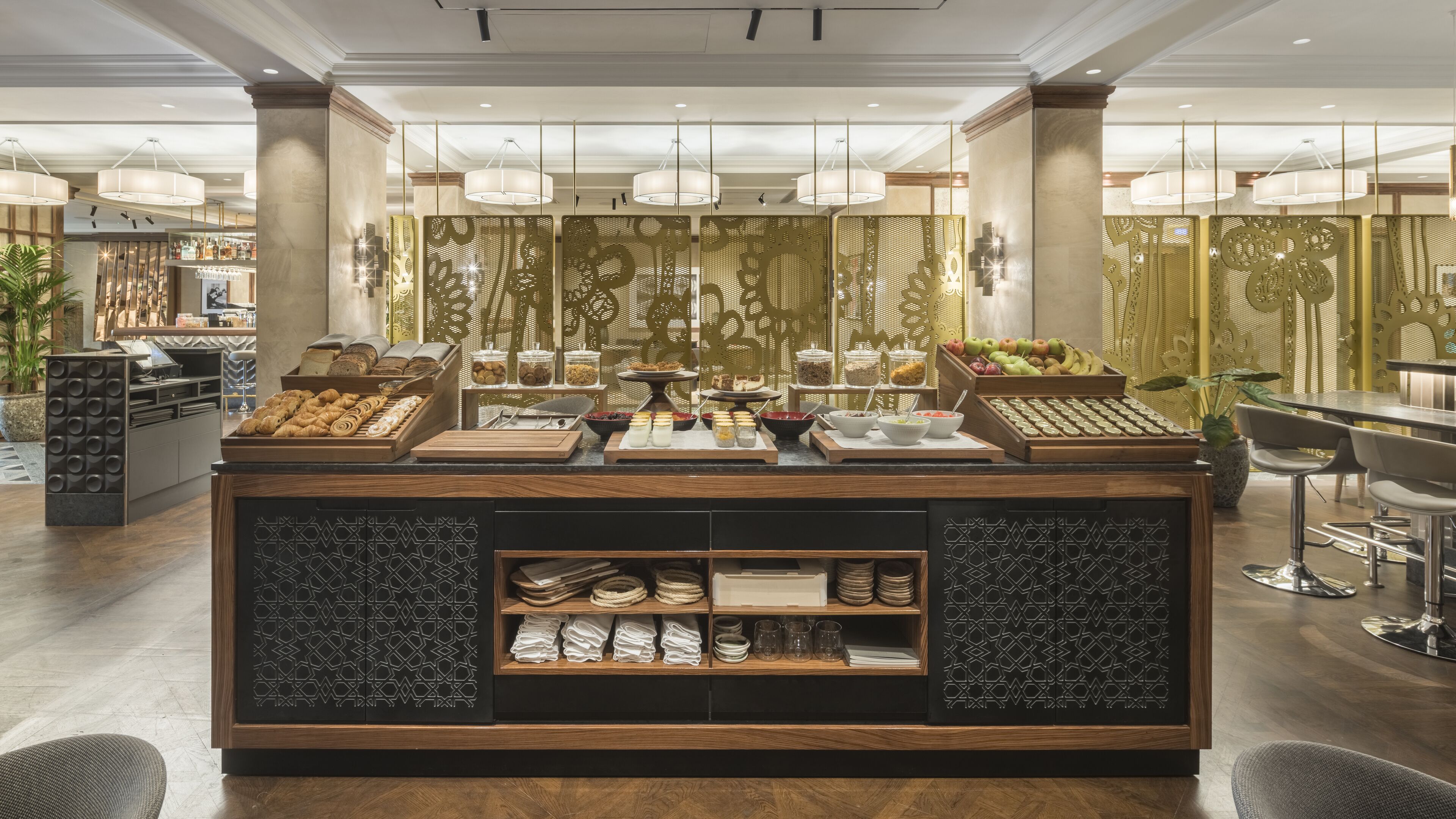 Un comptoir-déjeuner bien éclairé, proposant une variété de viennoiseries, de fruits et de boissons, le tout dans un cadre moderne agrémenté de coins salon.